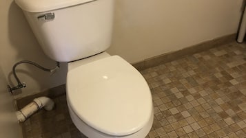 Lavabo blanc amb un rotlle de paper higiènic al dipòsit, una barana d'agafa a la paret i un sòl de rajoles.