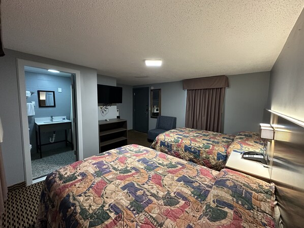 A hotel room with two beds, a desk, a chair, a TV, and a bathroom.