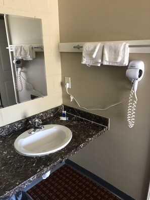 A bathroom with a sink, mirror, towel rack, hairdryer, and a hairdryer charging station.