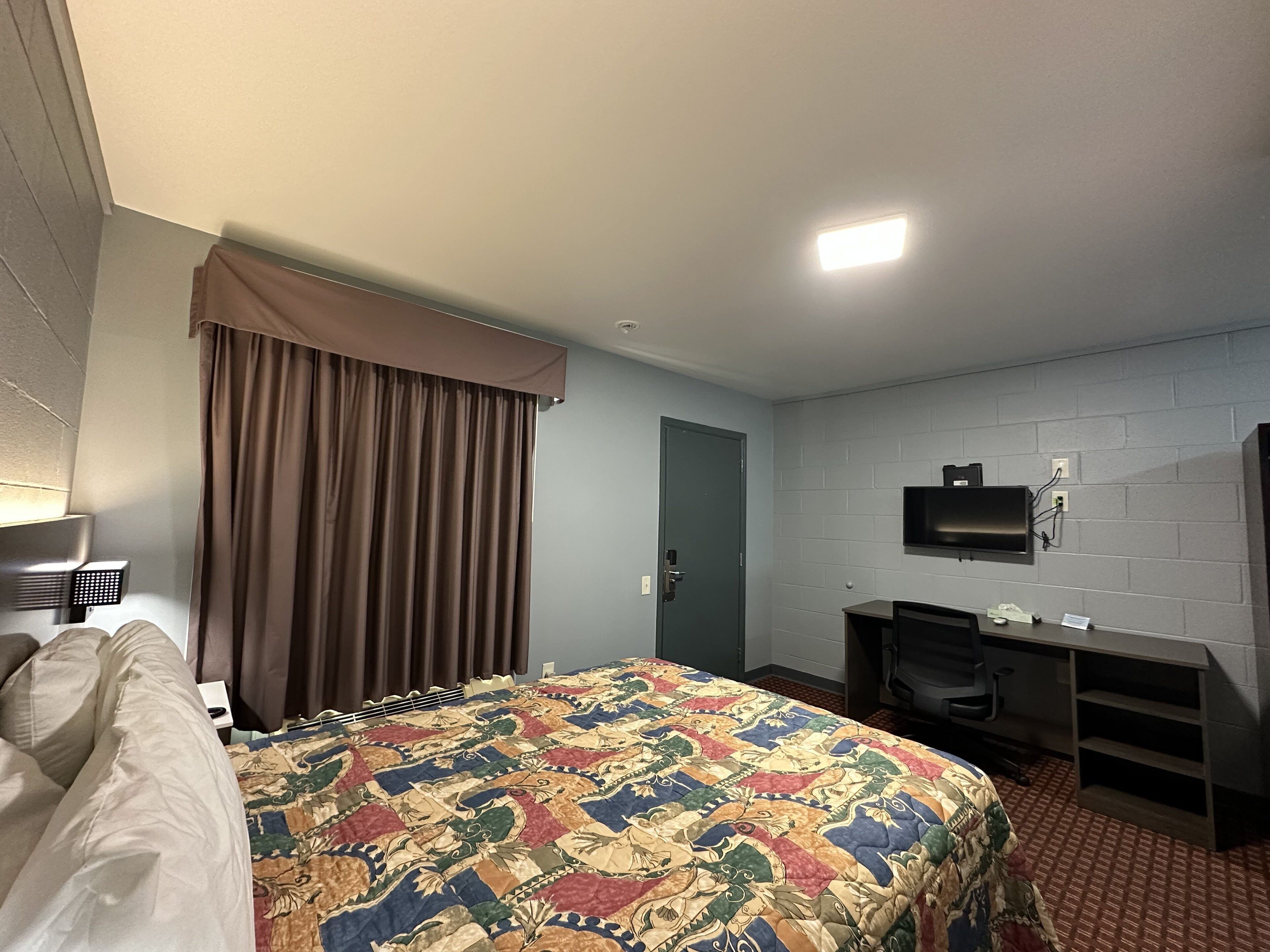 Une chambre d’hôtel avec un lit, un bureau, une télévision et une fenêtre avec des rideaux.