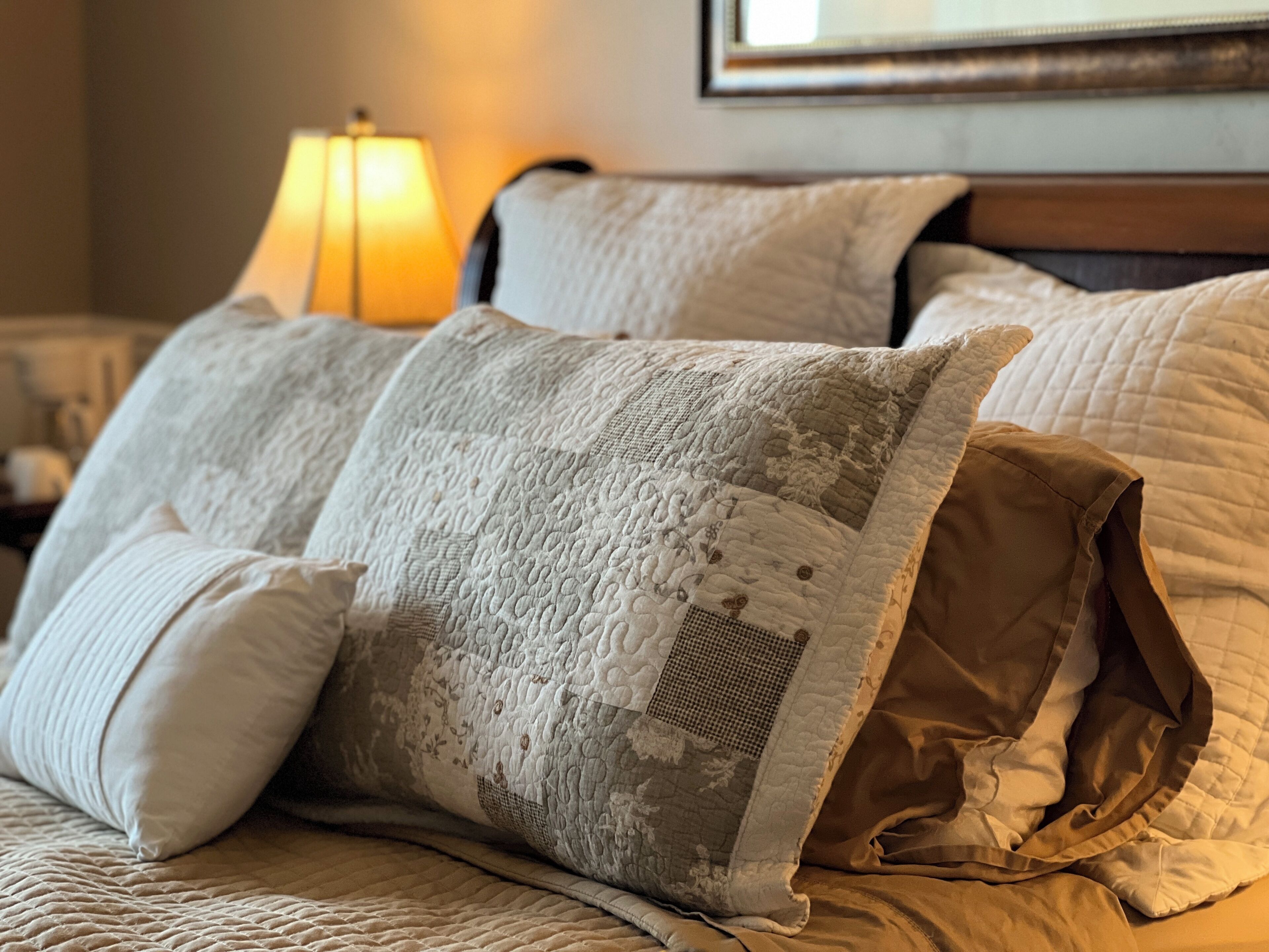 Una cama con varias almohadas, una lámpara y un cuadro en la pared.