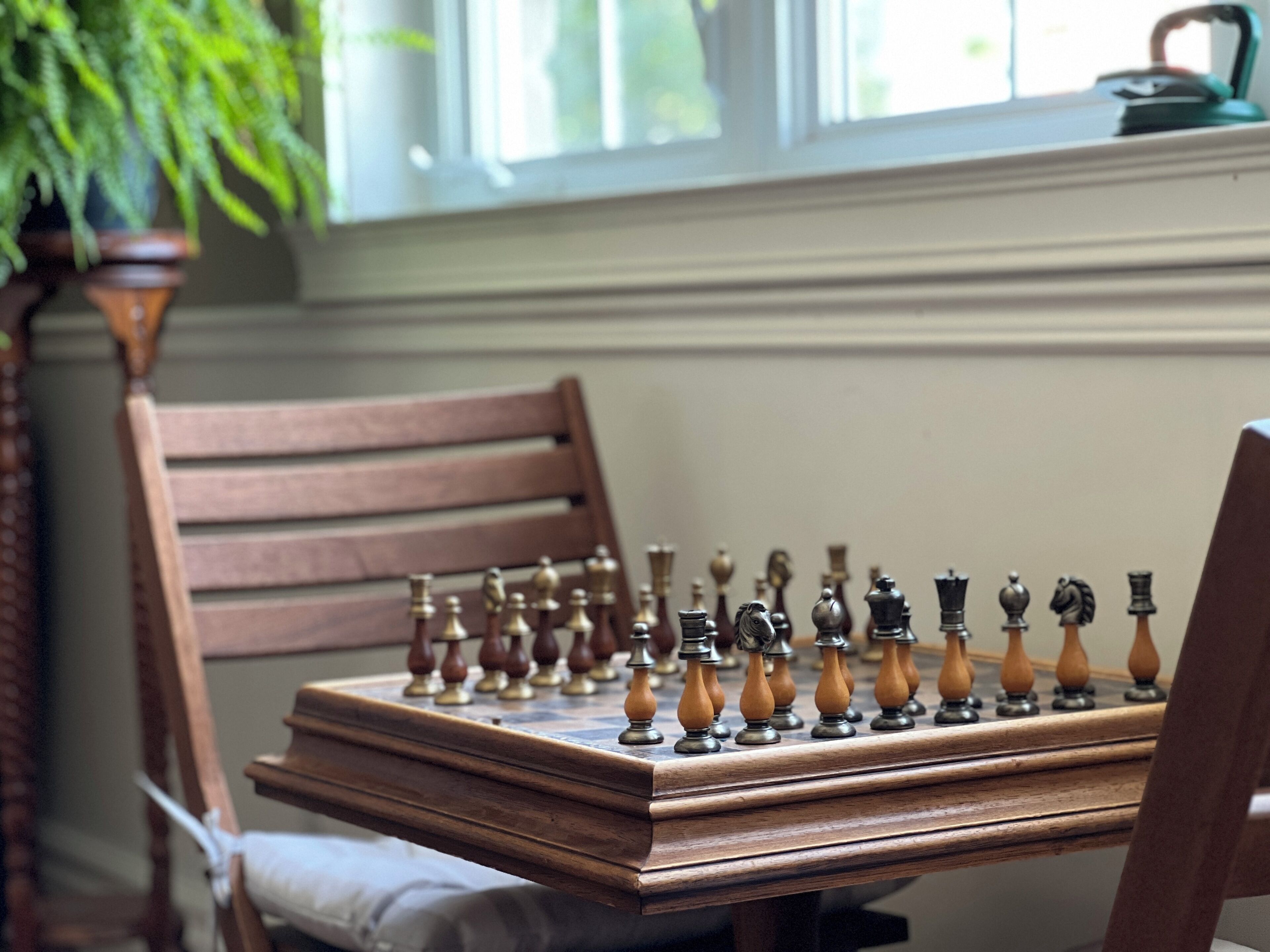 Un jeu d’échecs est posé sur une table en bois, avec une chaise à côté.