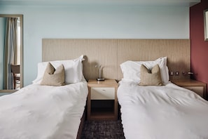 Una habitación de hotel con dos camas individuales, una mesita de noche con lámpara y un cabecero de madera.