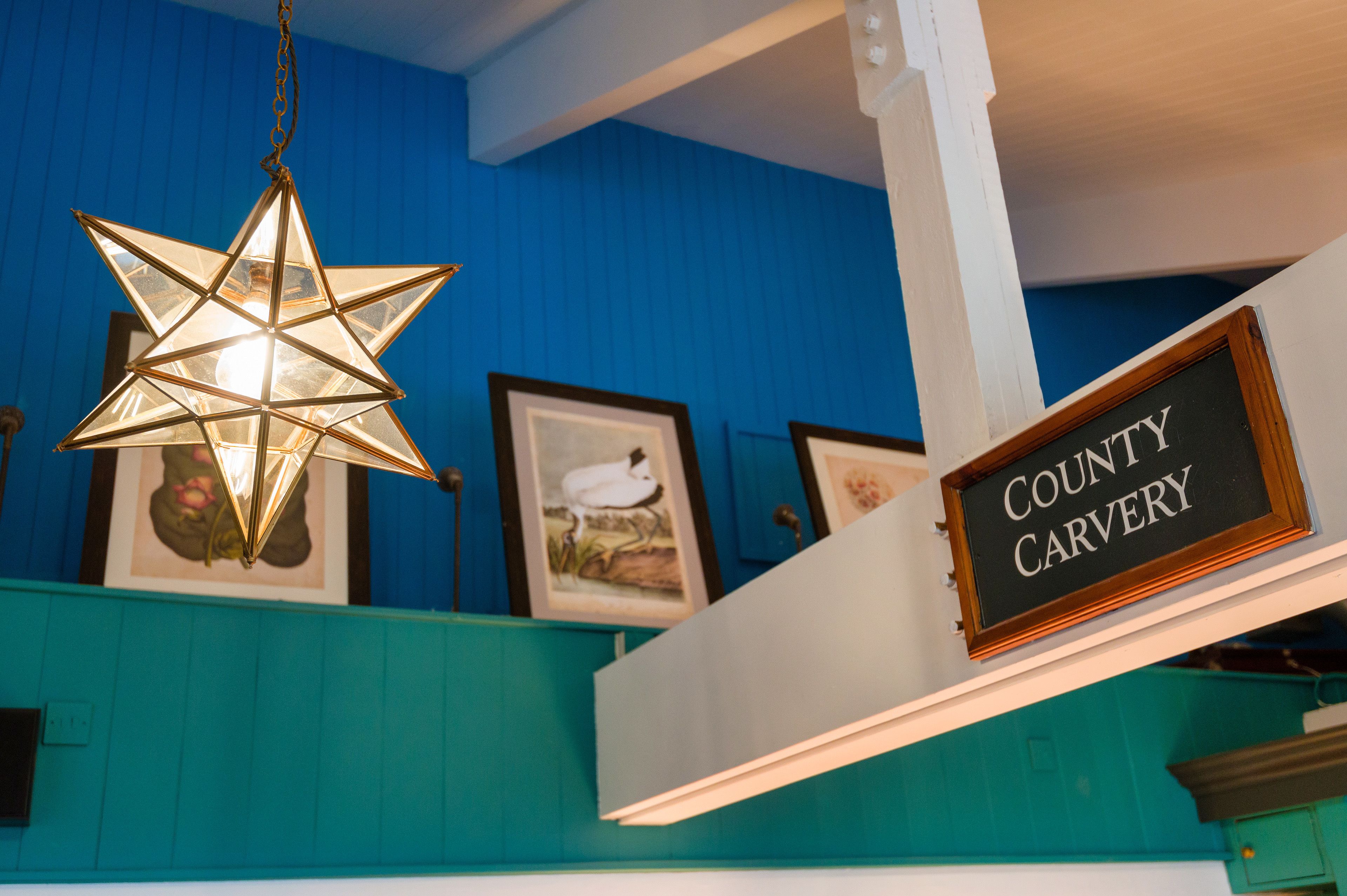 A star-shaped hanging light fixture, a framed sign reading "COUNTY CARVERY", and framed artwork on teal walls.
