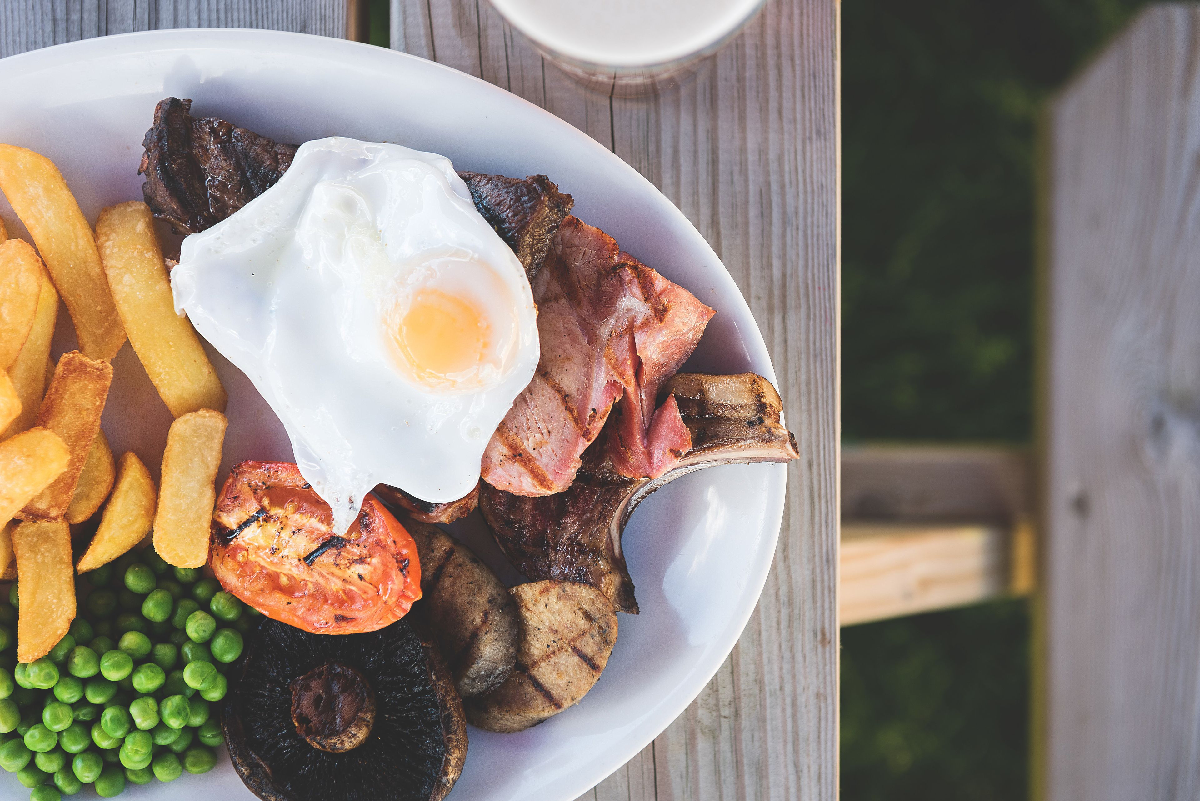 Une assiette contenant des œufs au plat, du bacon, des champignons, des tomates et des petits pois.