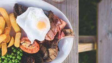 Une assiette contenant des œufs au plat, du bacon, des champignons, des tomates et des petits pois.