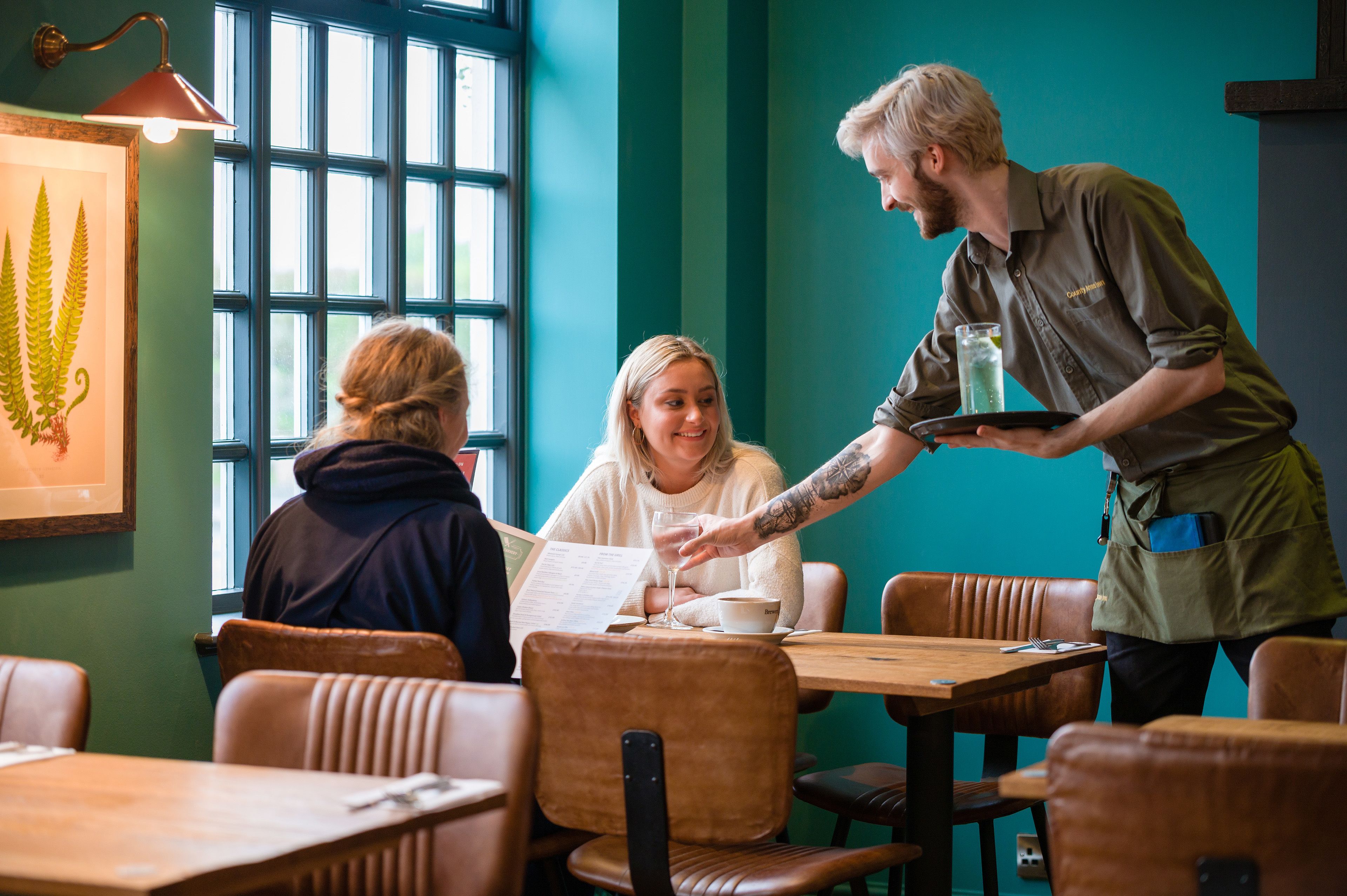 Un restaurant avec des tables et des chaises en bois, un menu et un serveur qui apporte une boisson.