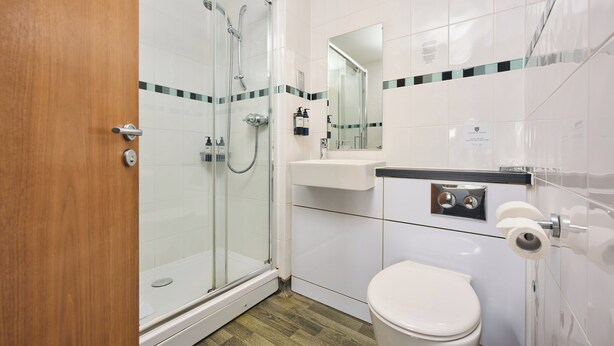 A bathroom with a glass-enclosed shower, a sink, a toilet, and a mirror. - County Arms (Truro)
