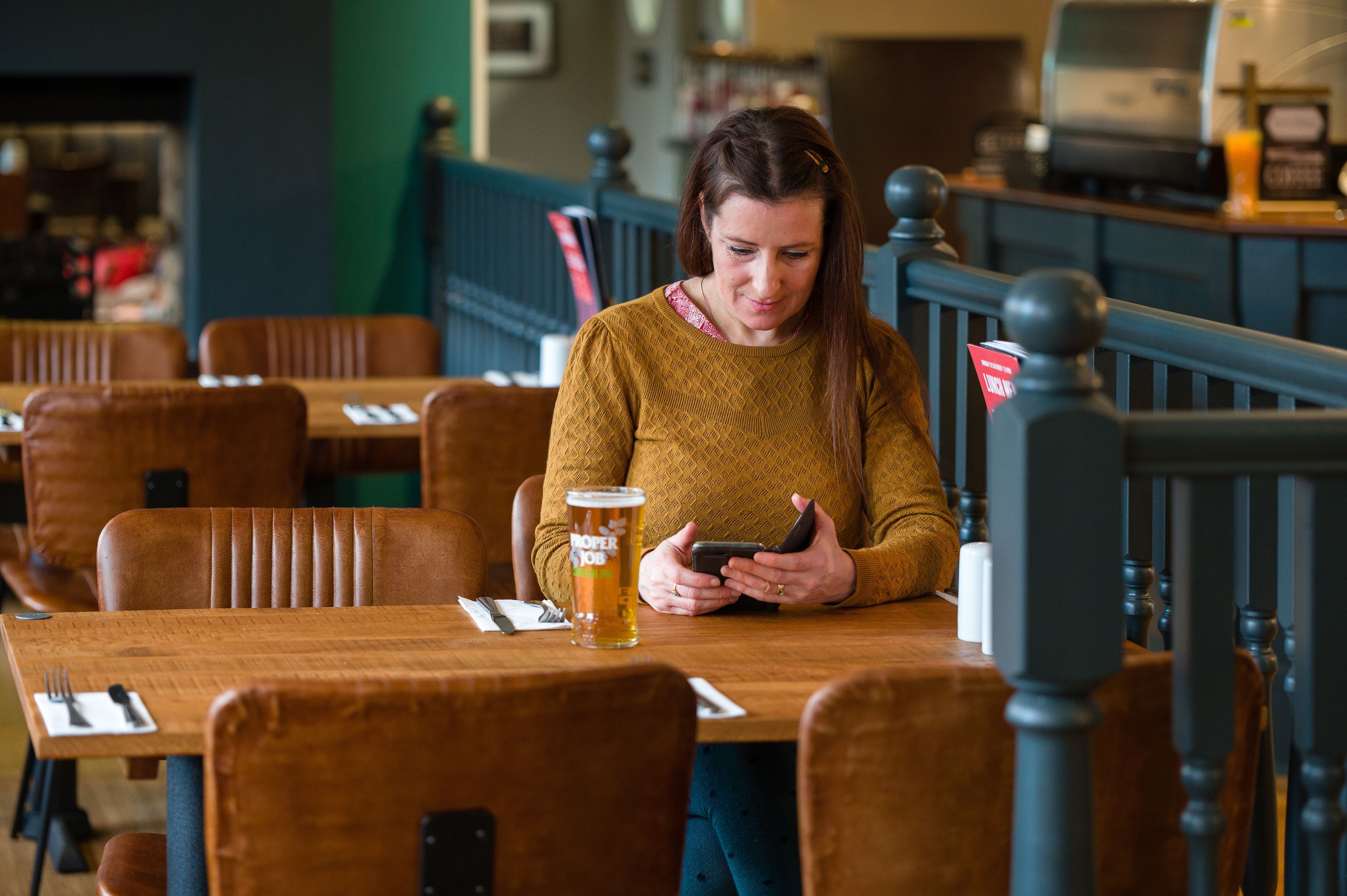 Una persona sentada a una mesa de madera con una jarra de cerveza y un teléfono inteligente.