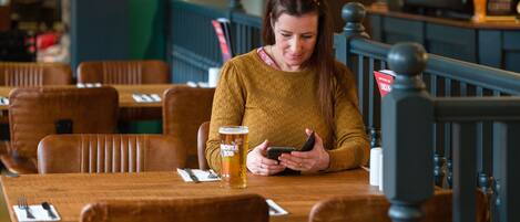 Una persona sentada a una mesa de madera con una jarra de cerveza y un teléfono inteligente.
