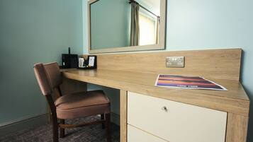 A hotel room with a wooden desk, a chair, a mirror, a small black radio, and a picture frame.