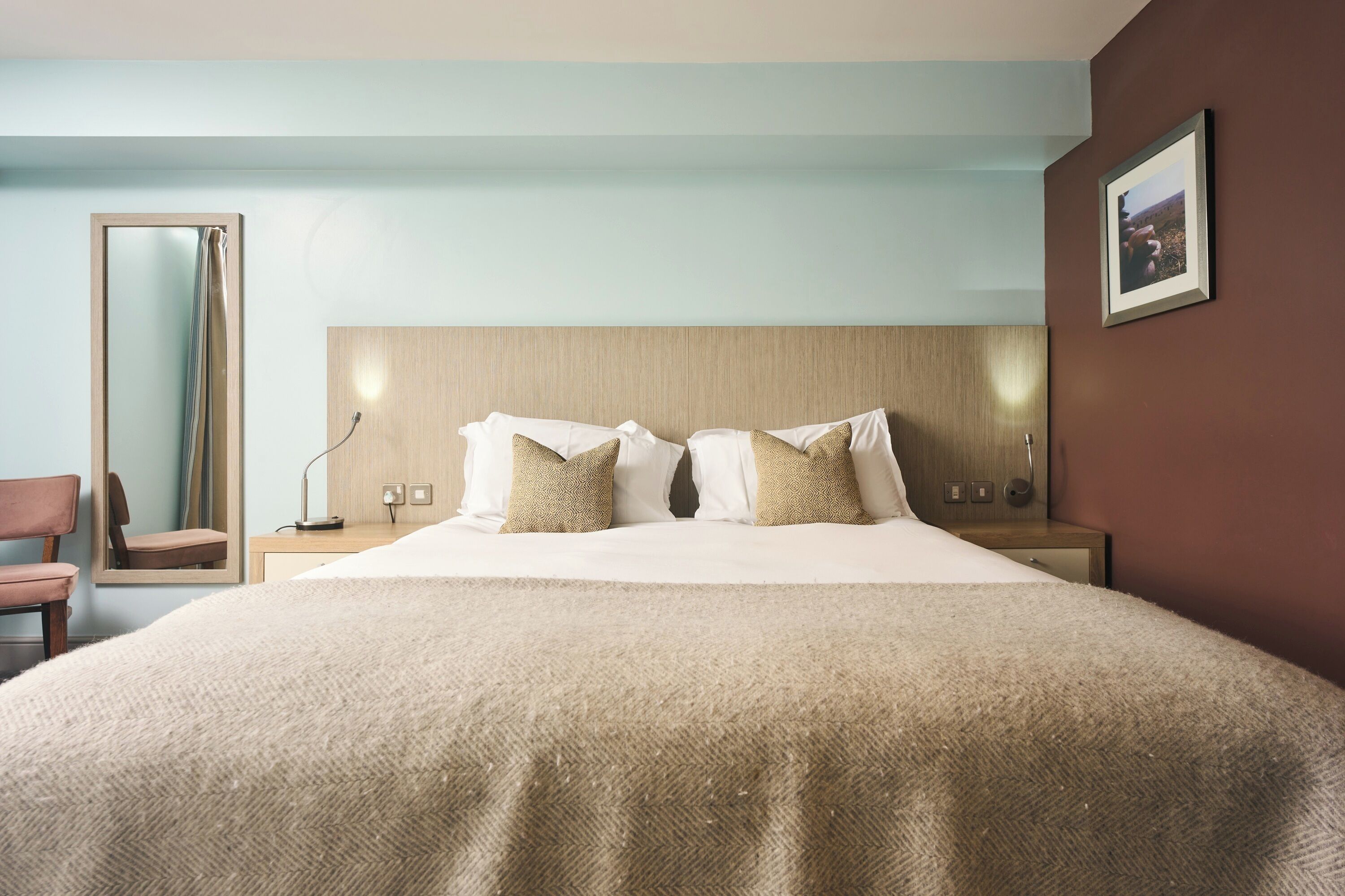 Ein Hotelzimmer mit einem großen Bett, einem Nachttisch, einem Spiegel und einem Sessel.