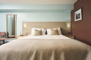 Habitación de hotel con una cama grande, una mesita de noche, un espejo y una silla.