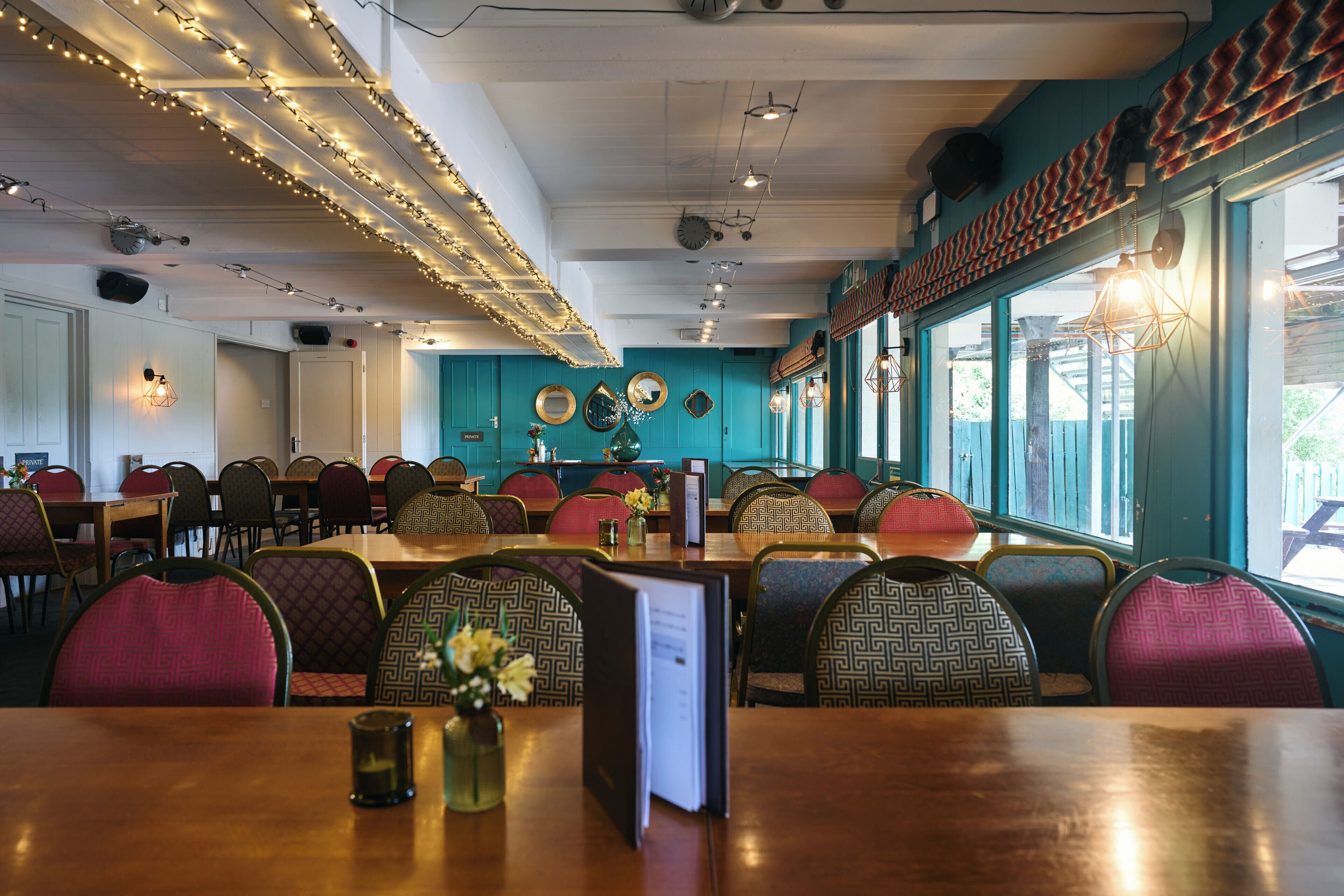 A restaurant interior with multiple dining tables, chairs, and a view through large windows.
