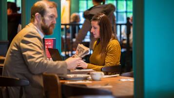 A person handing over a menu to another person at a table in a cafe.
