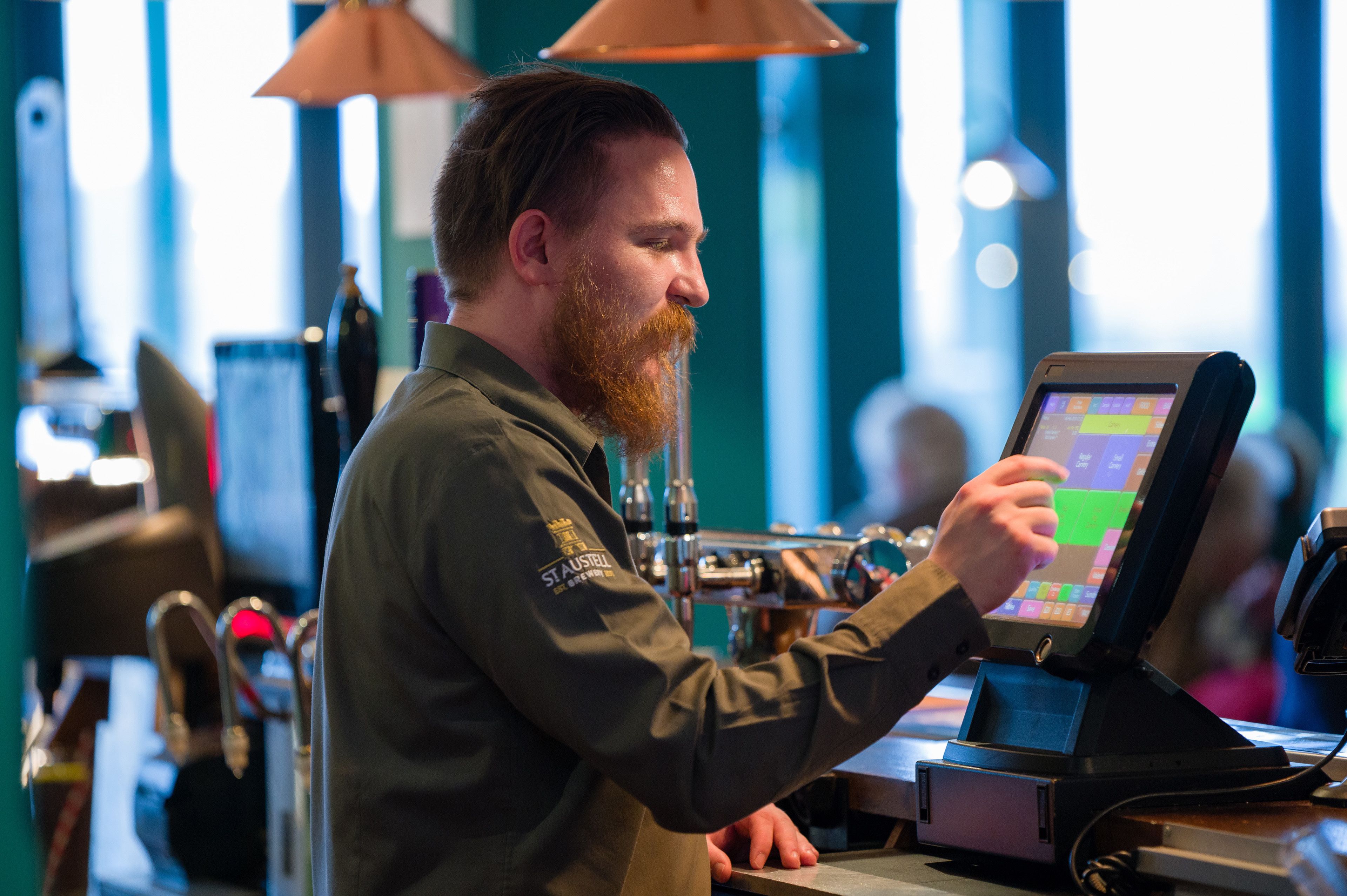 A person using a touchscreen device at a counter in a brightly lit indoor setting.