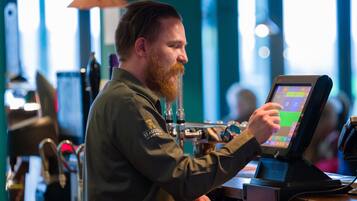 A person using a touchscreen device at a counter in a brightly lit indoor setting.