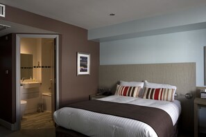 Comfortable retreat with a large bed, bedside table, and framed picture.