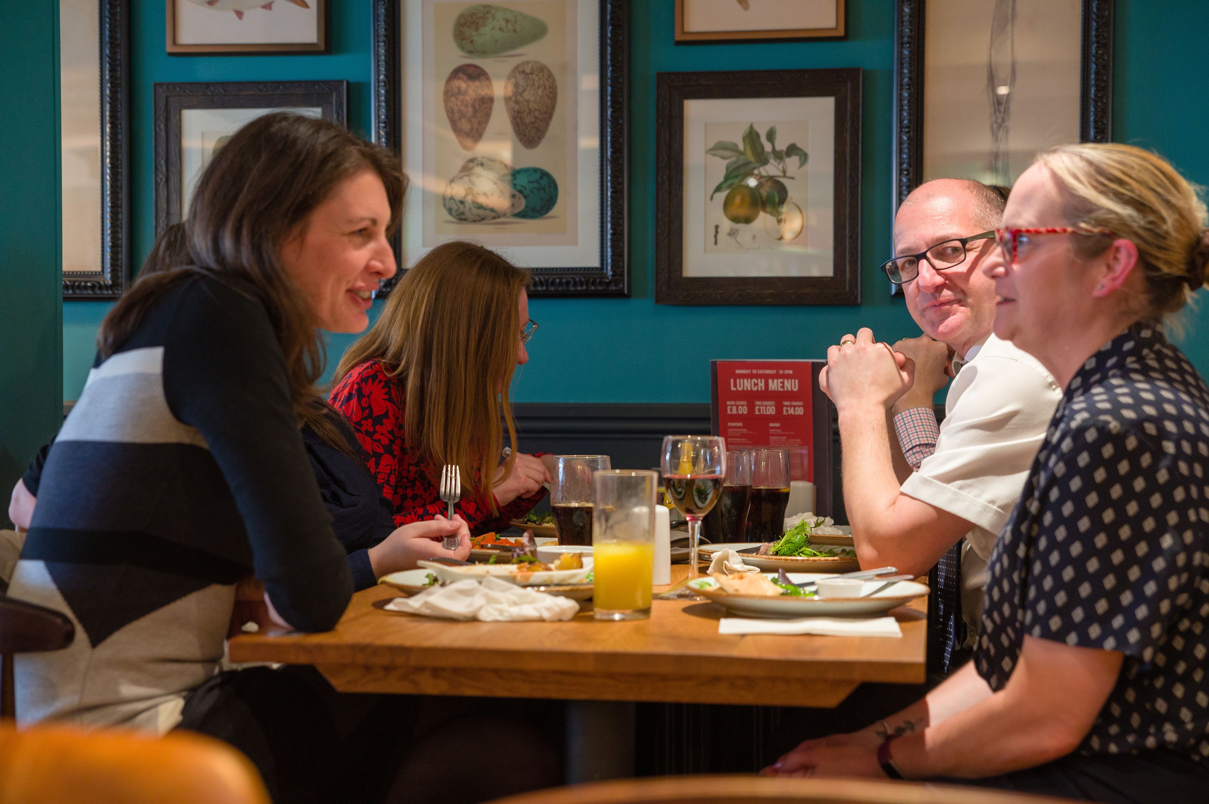 A group of people dining at a restaurant with framed artwork on the wall.