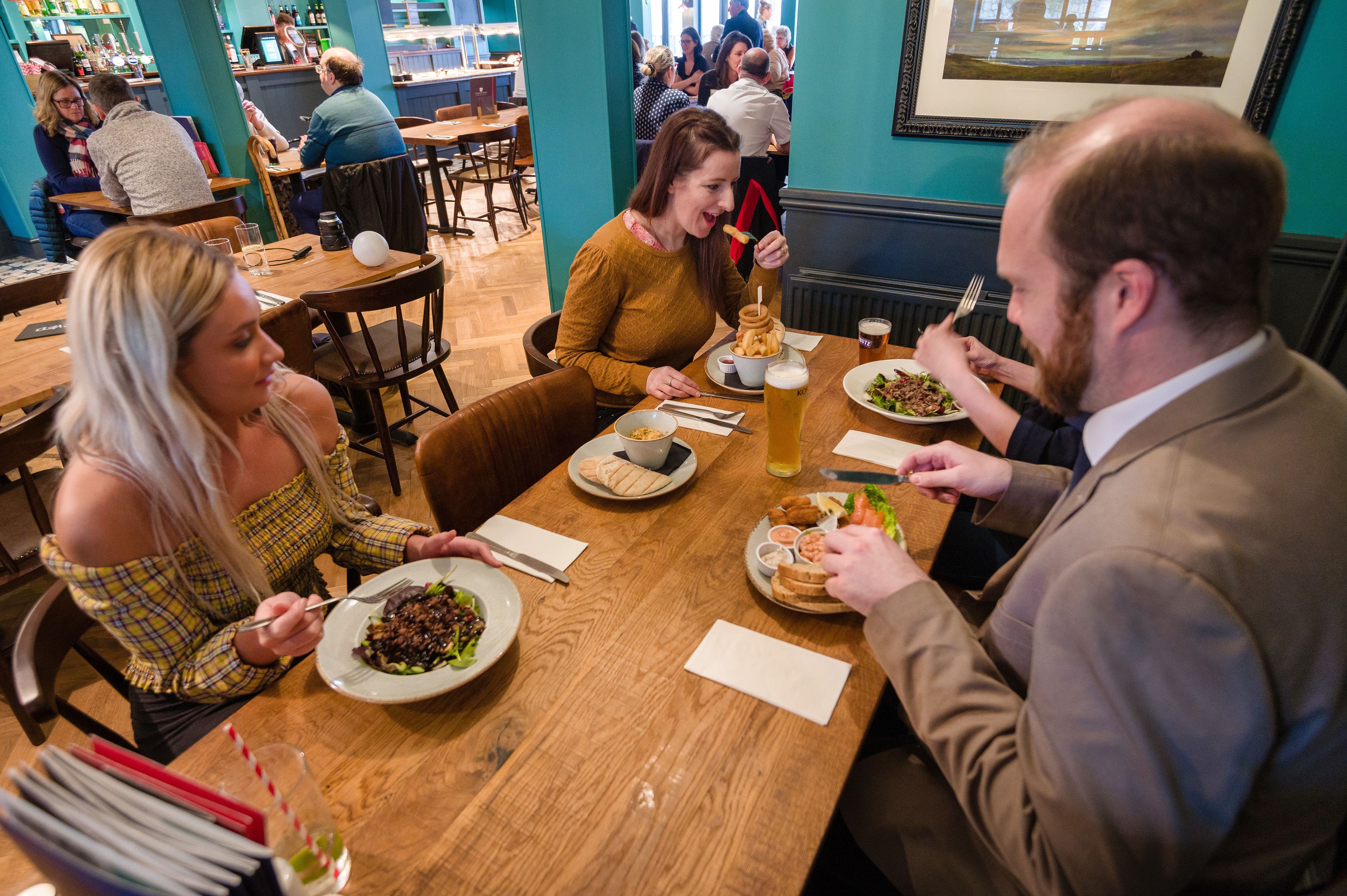 Un restaurant avec des tables et des chaises en bois, des clients assis et une variété de plats servis.