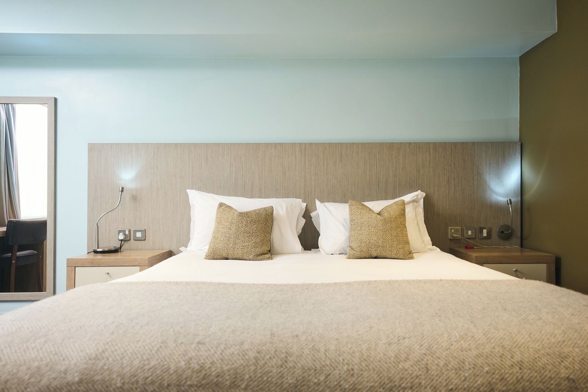 Een hotelkamer met een groot bed, twee nachtkastjes, een lamp en een spiegel.
