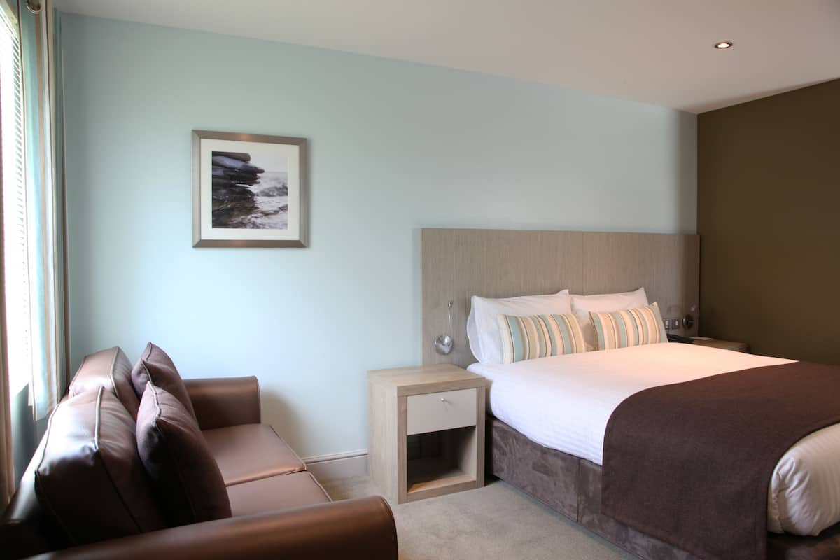 A hotel room with a bed, a nightstand, a chair, and a framed picture on the wall.