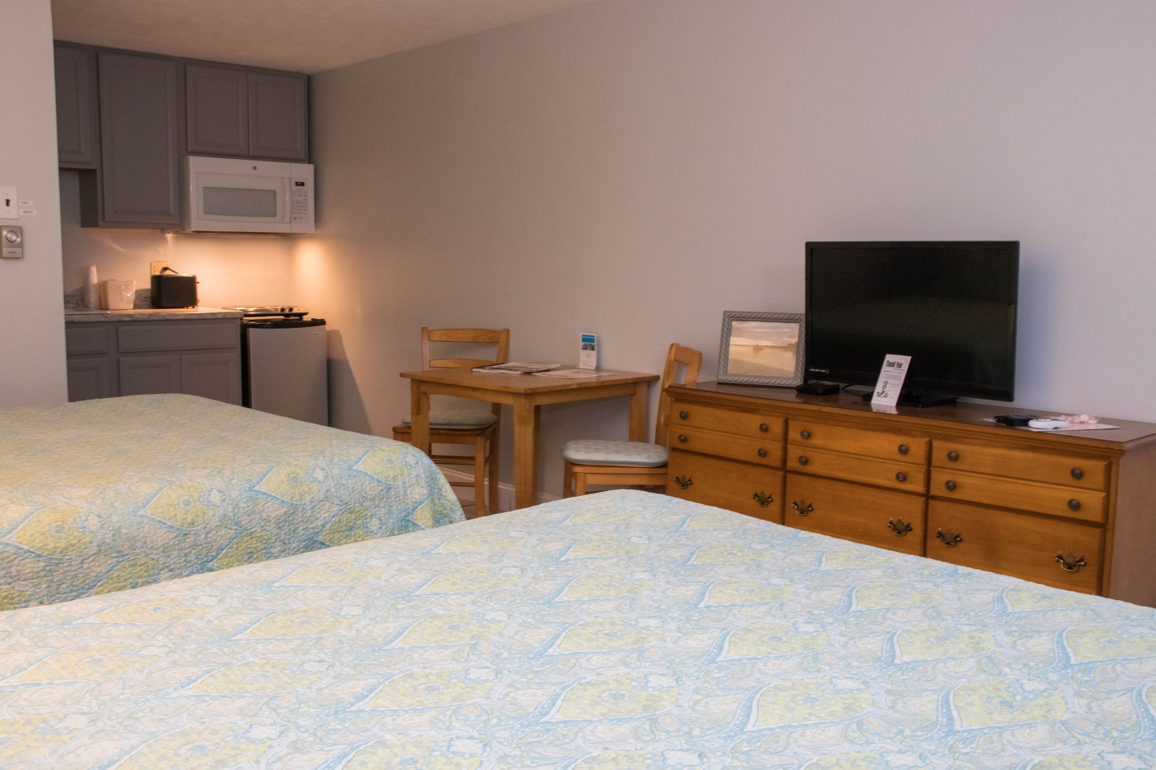 A room with two beds, a wooden desk with a computer, a television, and a microwave.