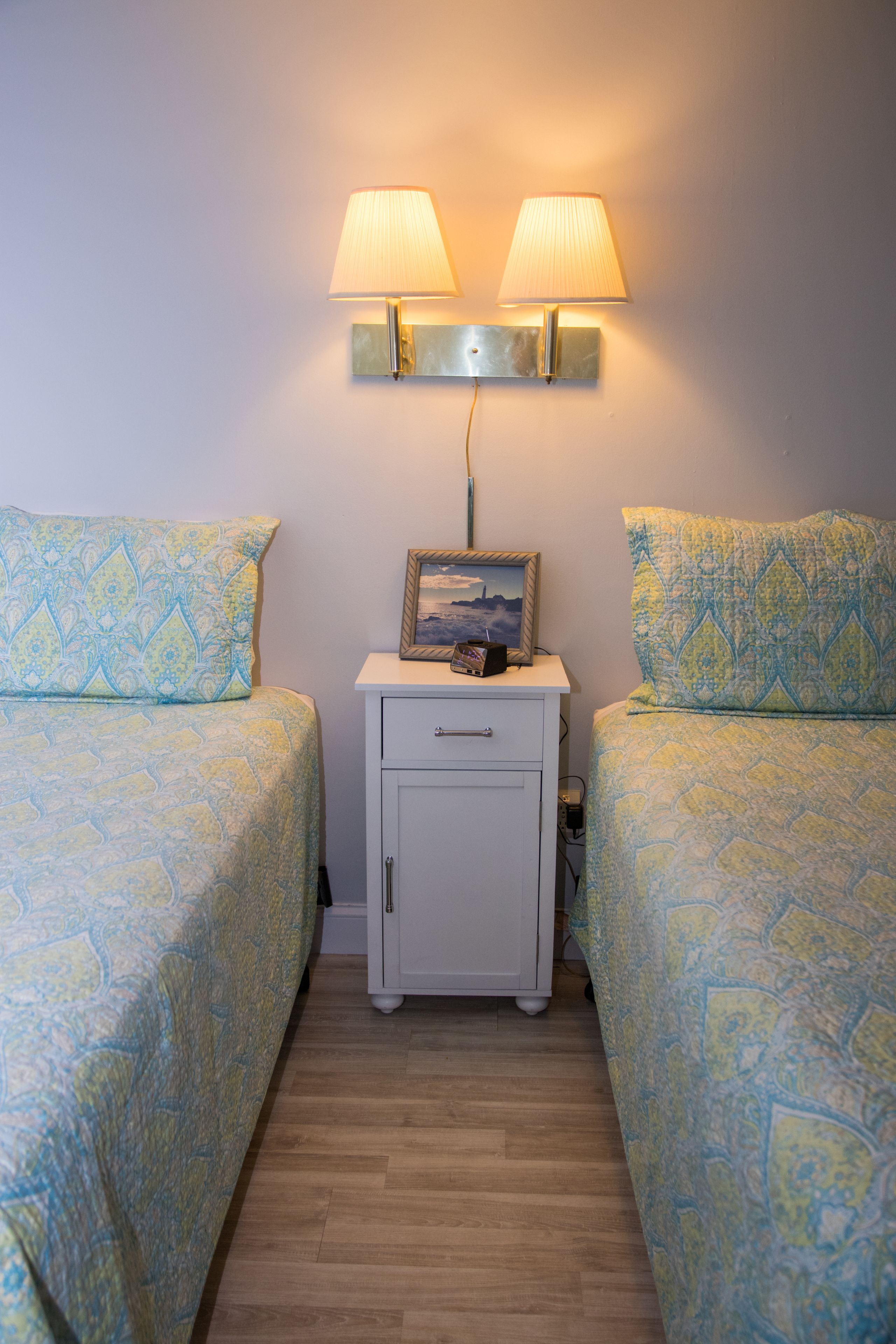 A bedroom with two beds, a nightstand with a lamp, and a small cabinet.
