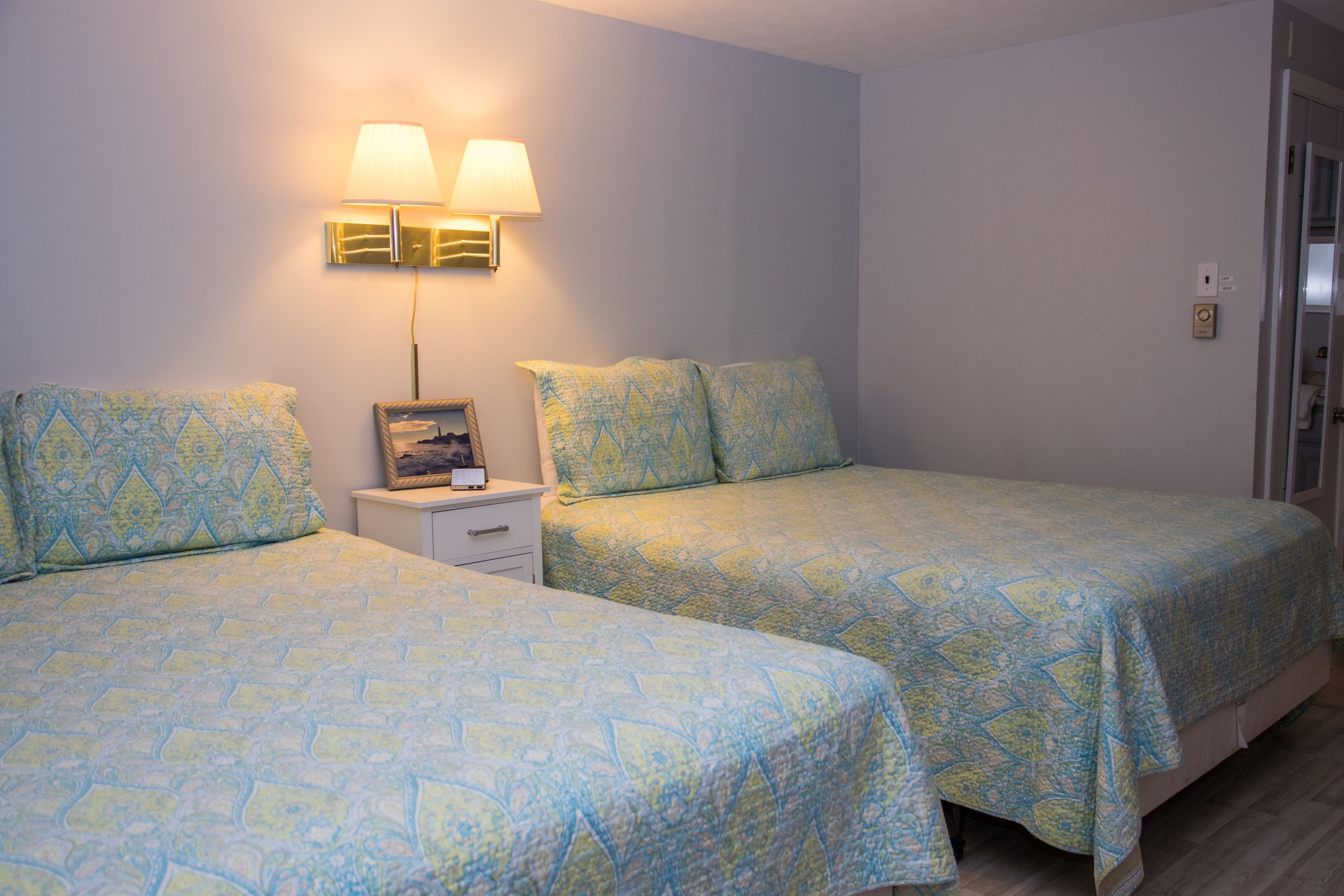 Habitación de hotel con dos camas, una mesita de noche, una lámpara y una puerta.