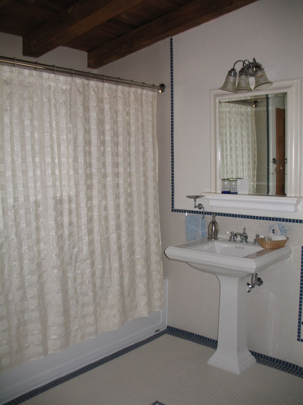 A bathroom with a shower curtain, a sink with a mirror, and a tiled floor.