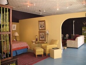 Een kamer met een bed, twee stoelen, een bank, een lamp en een boekenplank.