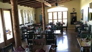 A spacious dining area with wooden tables and chairs, large windows, and a high ceiling with exposed beams. - Bear Mountain Lodge (Silver City)