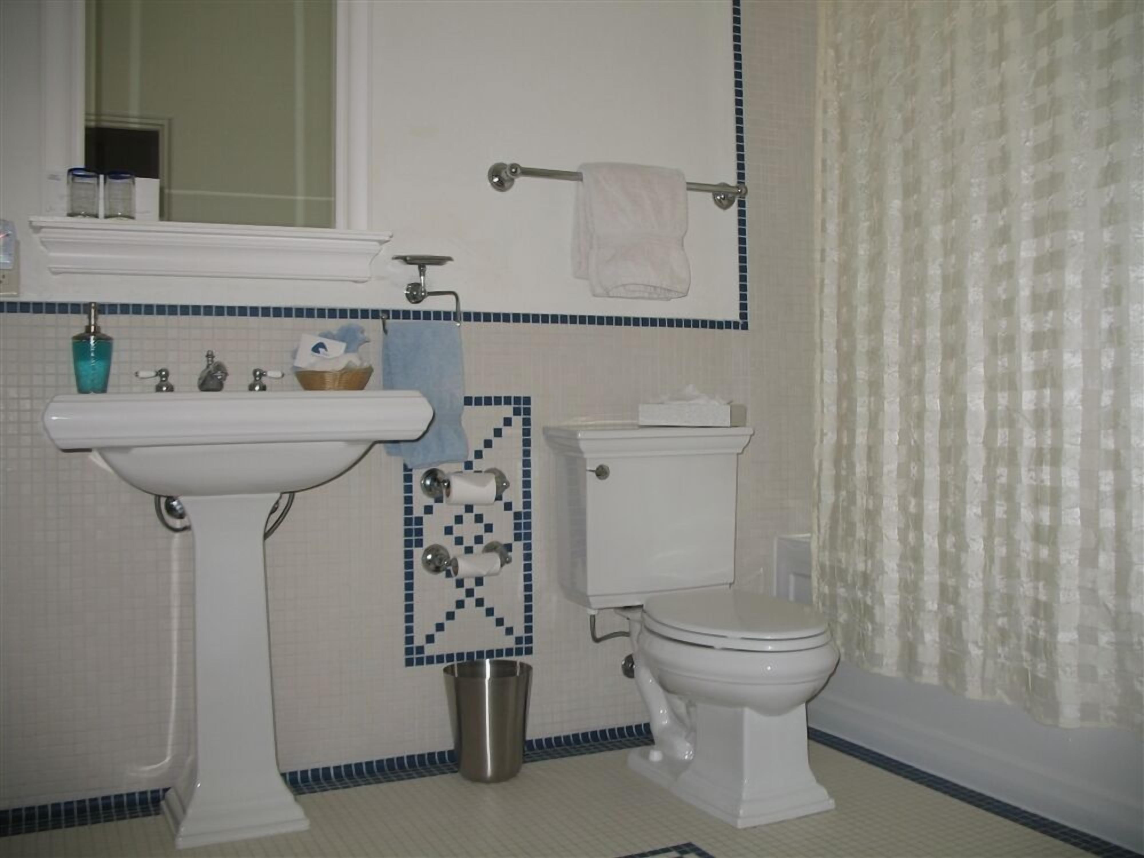 A bathroom with a pedestal sink, toilet, and a small trash can.