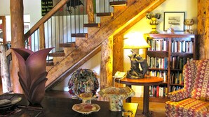 A cozy living room with a wooden staircase, a bookshelf, and various decorative items. - Bear Mountain Lodge (Silver City)