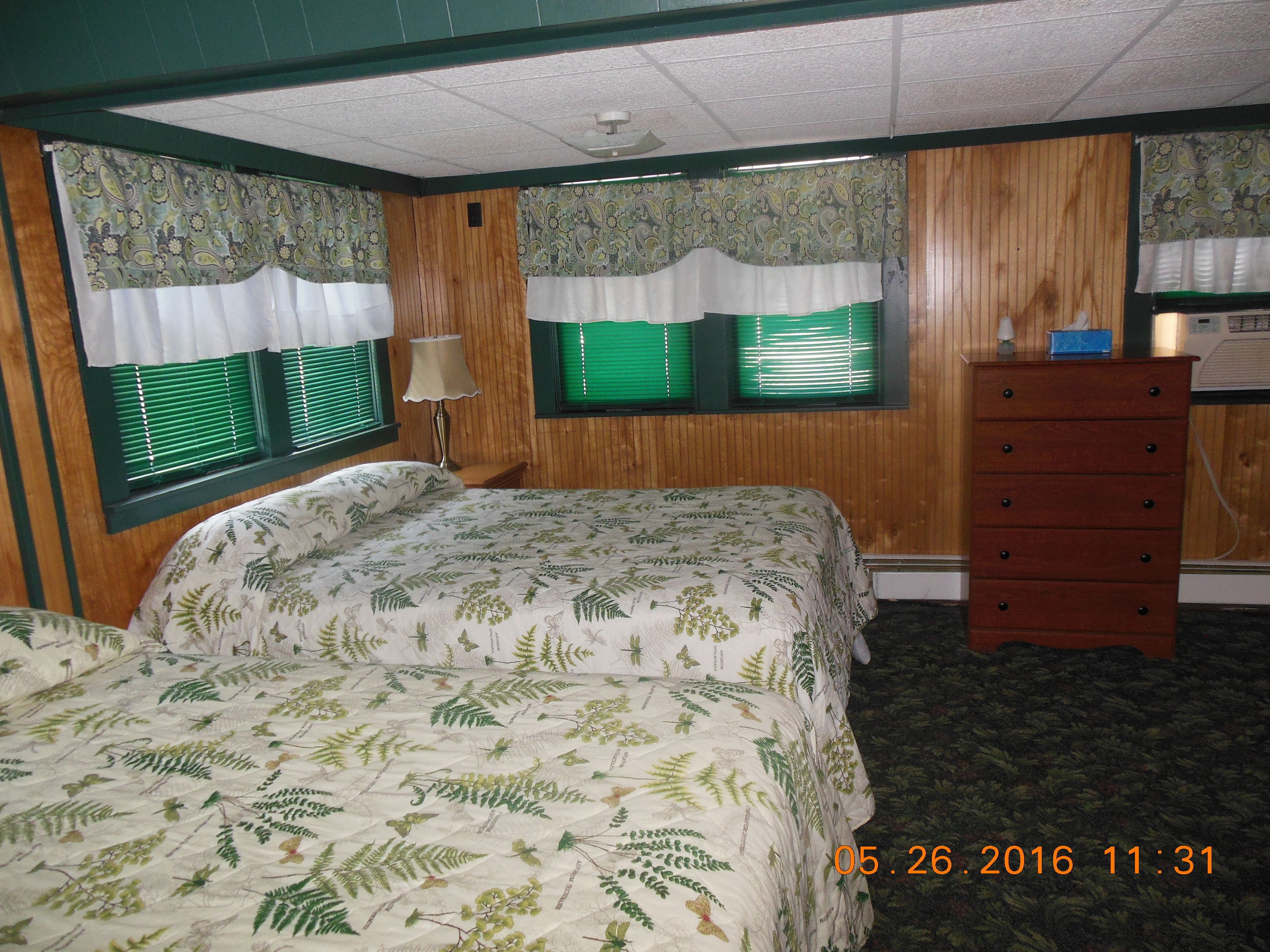 Quarto com cama, penteadeira e duas janelas com persianas verdes.