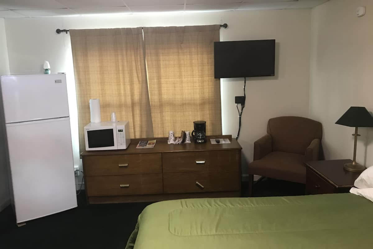 A hotel room with a bed, a dresser, a microwave, a coffee maker, a television, and a chair.