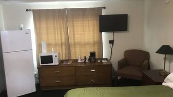 A hotel room with a bed, a dresser, a microwave, a coffee maker, a television, and a chair.