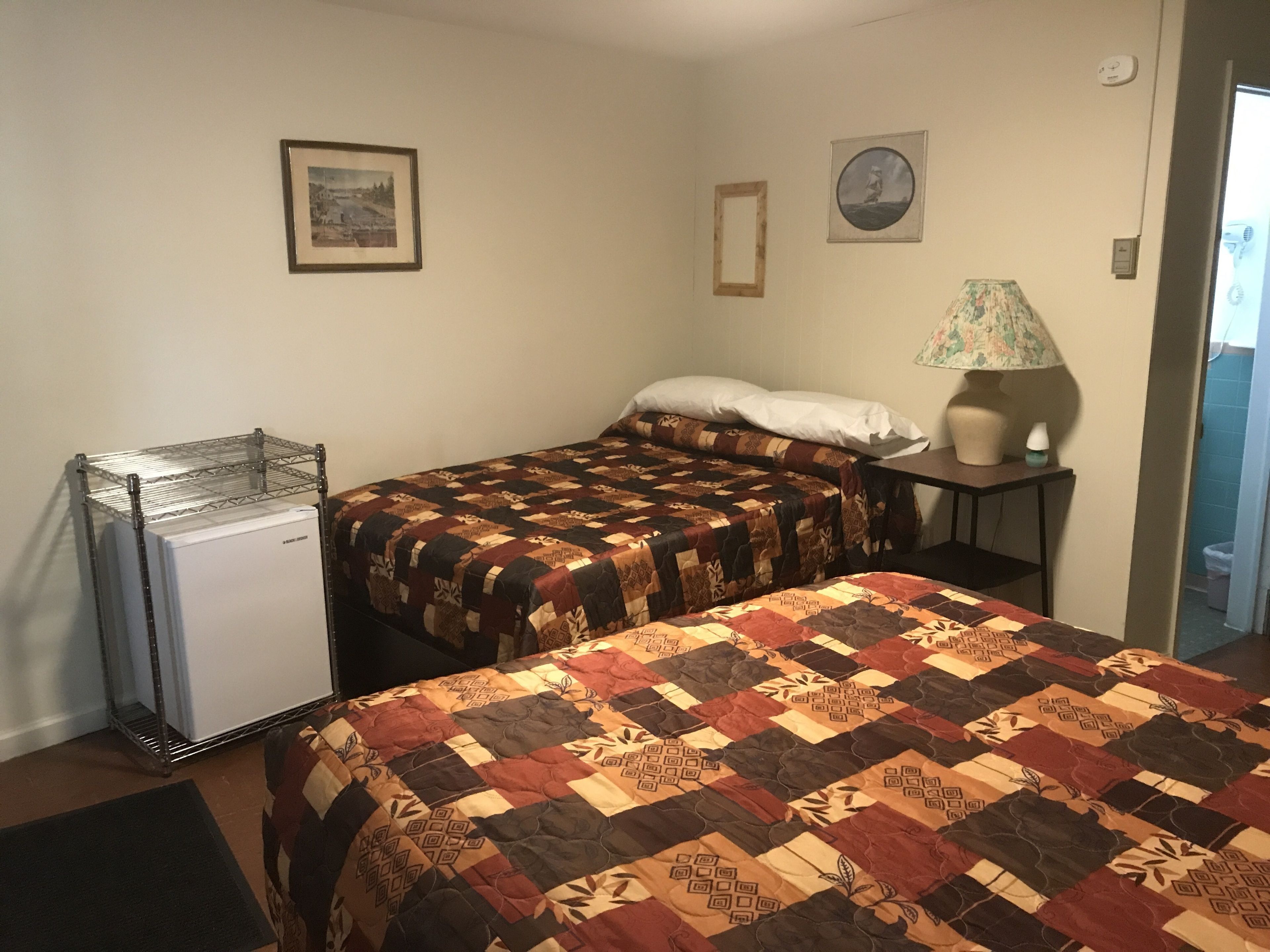A room with two beds, a small refrigerator, a lamp, and a picture on the wall.