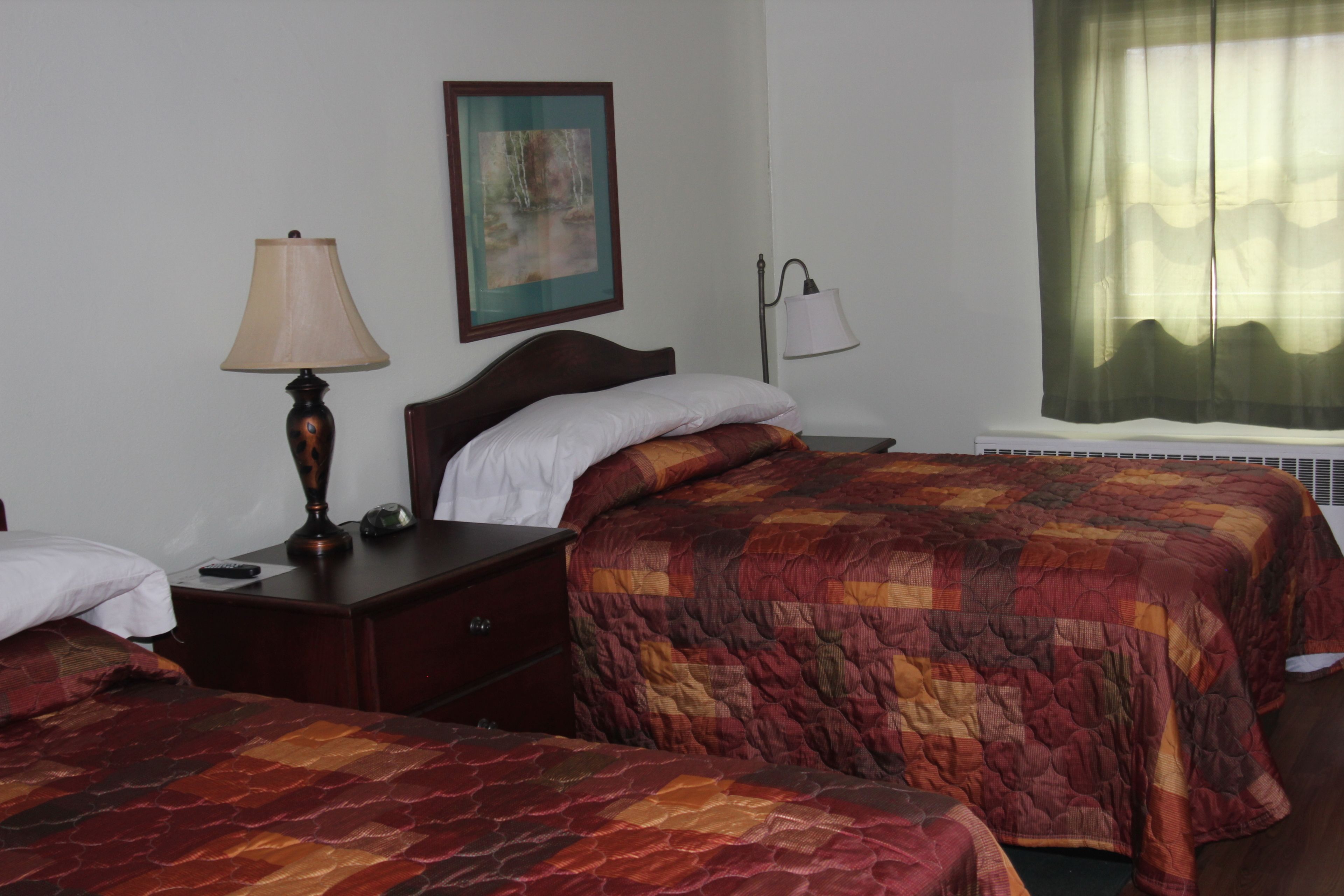 A hotel room with two beds, a nightstand, a lamp, a painting, and a window with curtains.