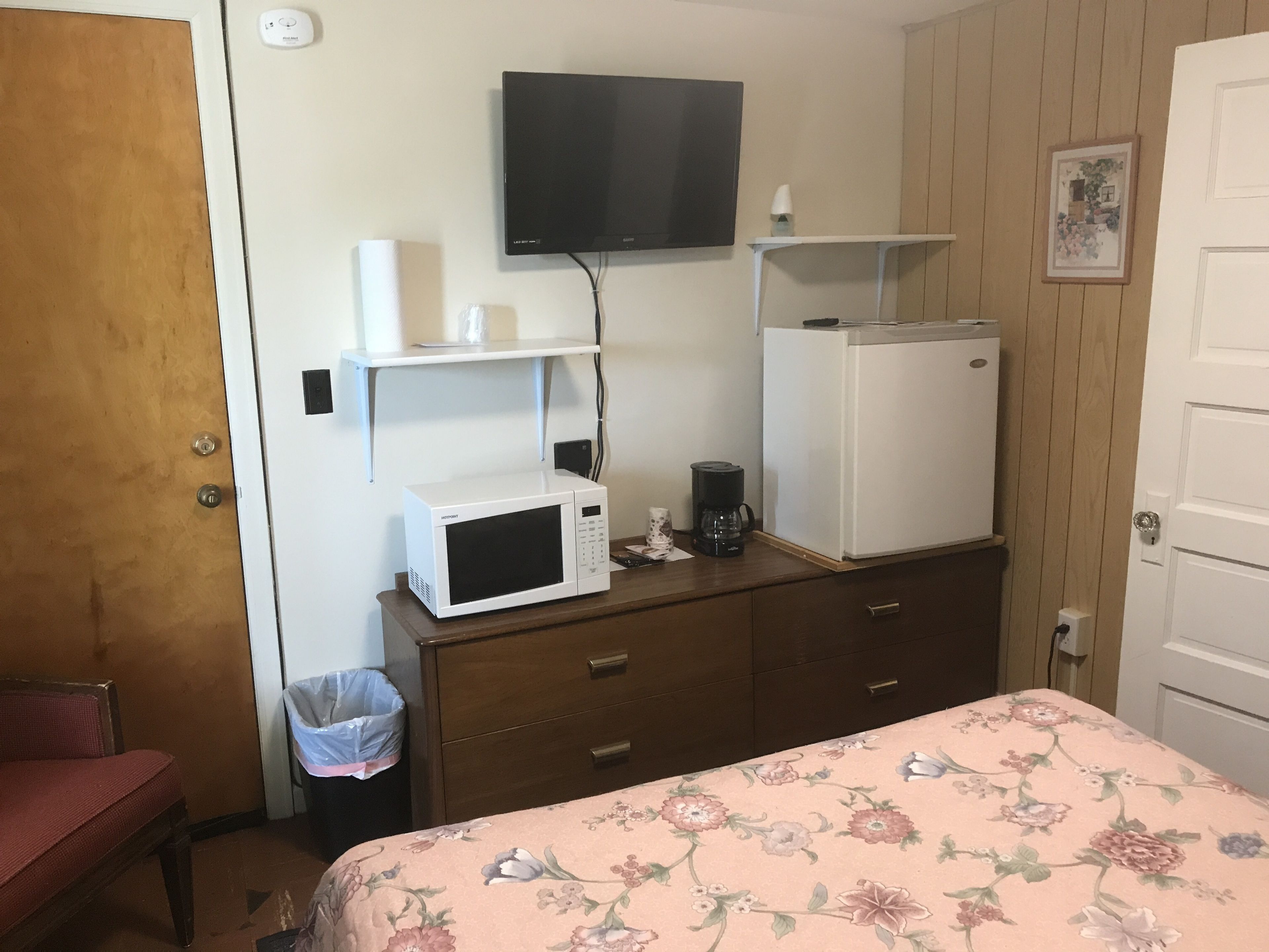Habitación de hotel con una cama, microondas, refrigerador, televisor montado en la pared y un armario de madera.