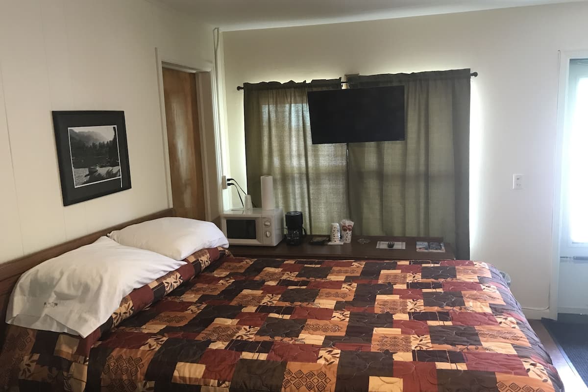 A bedroom with a bed, a framed picture on the wall, a microwave, and a window with curtains.