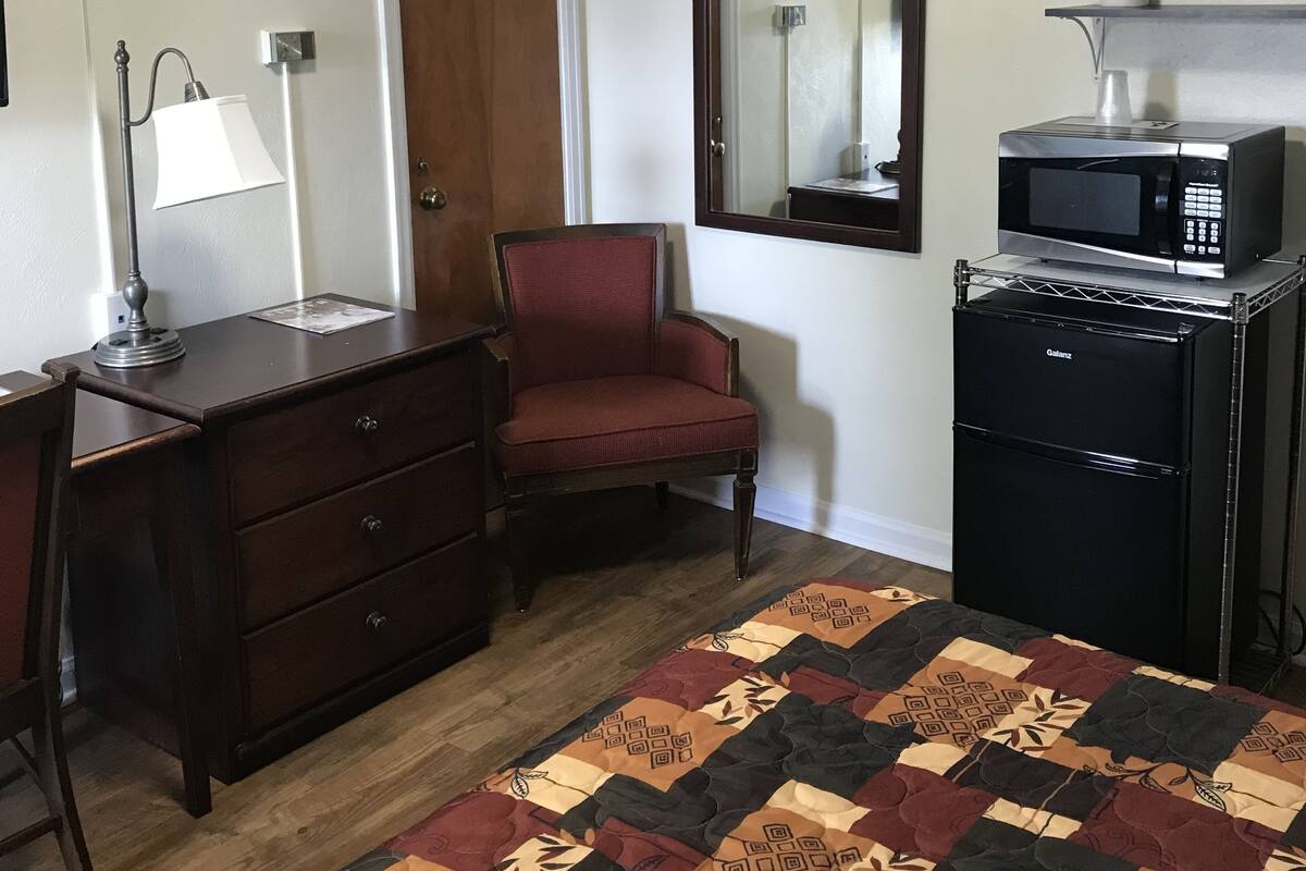 A compact room with a wooden dresser, a red chair, a small black refrigerator, a microwave, and a patterned rug.