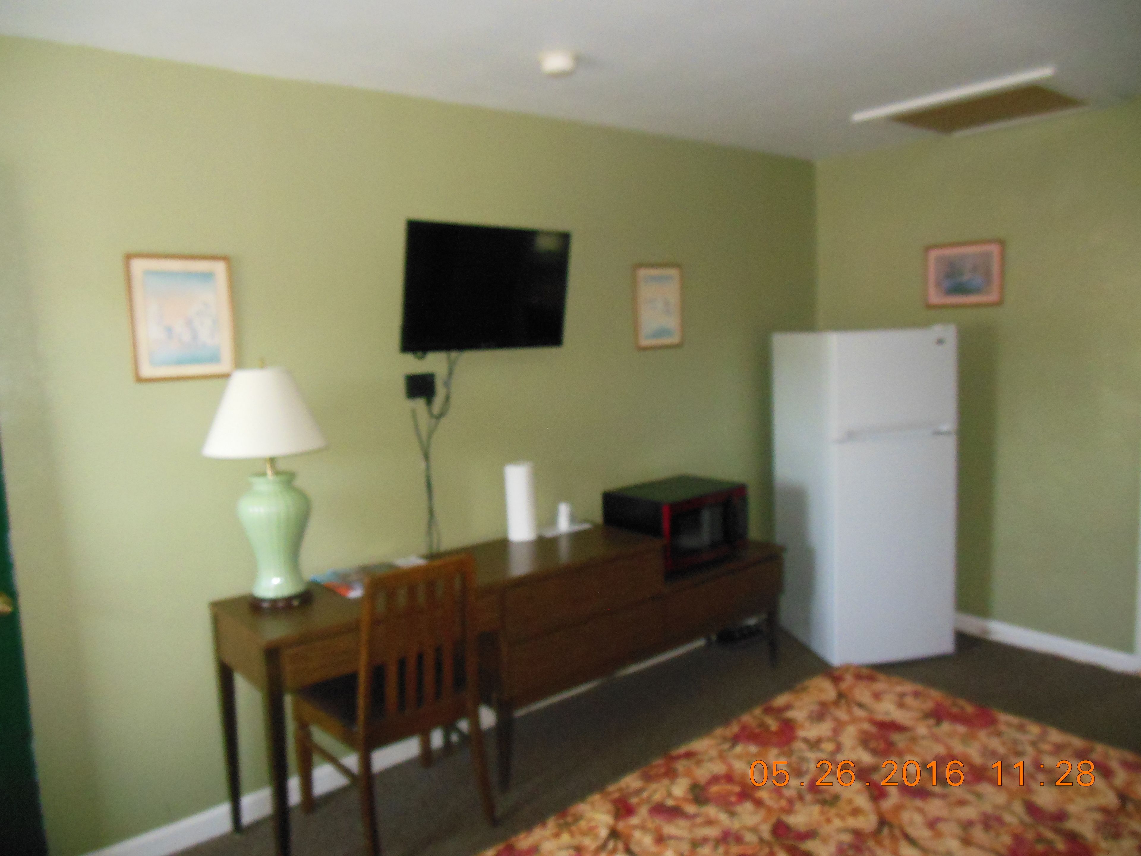 A room with a desk, chair, television, and a refrigerator.