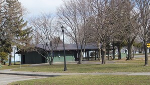 A park with a gazebo, trees, and a building with a green roof. - The Evergreen Motel (Oswego)