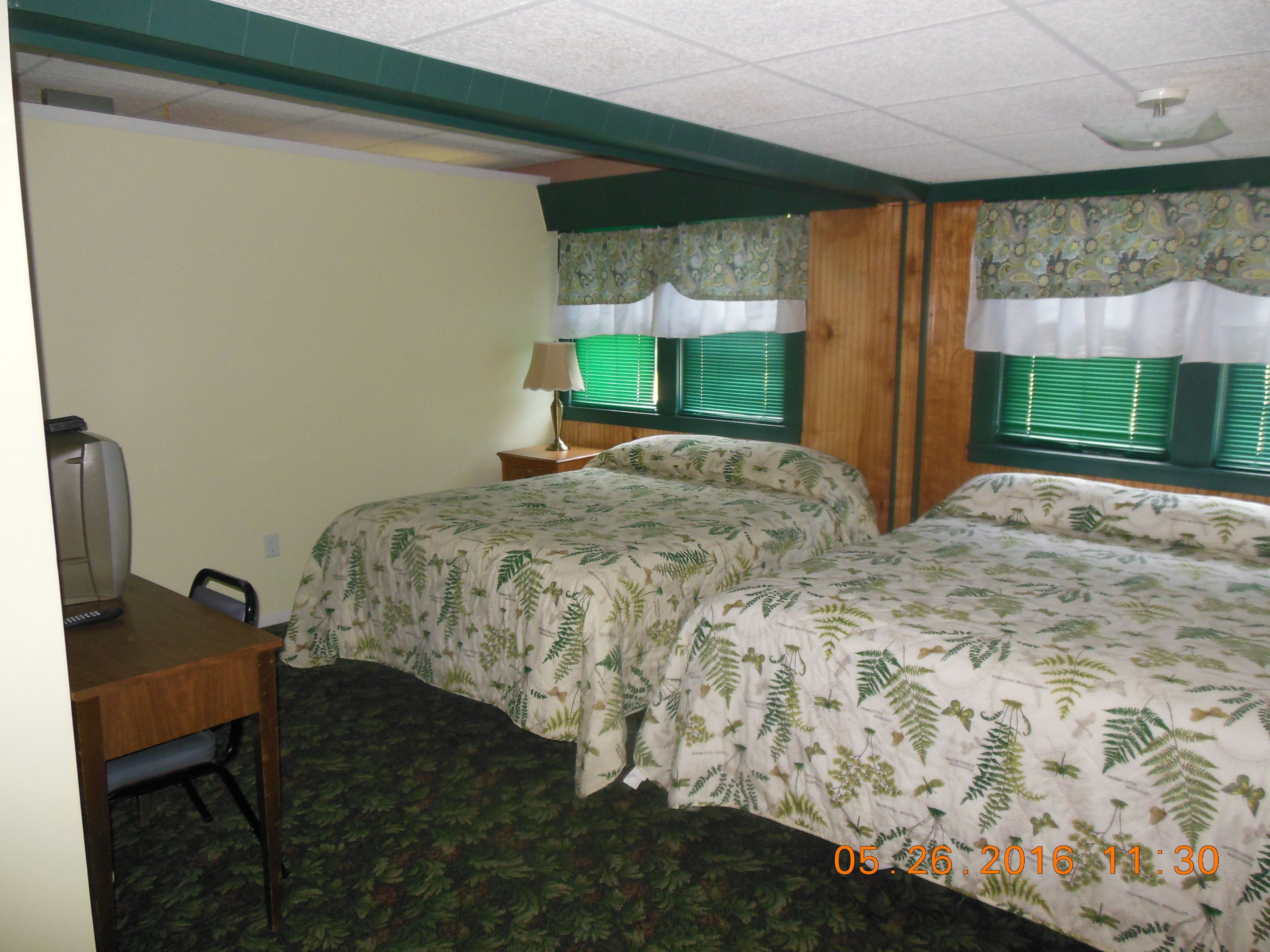 A hotel room with two beds, a desk, a chair, a lamp, and a television.