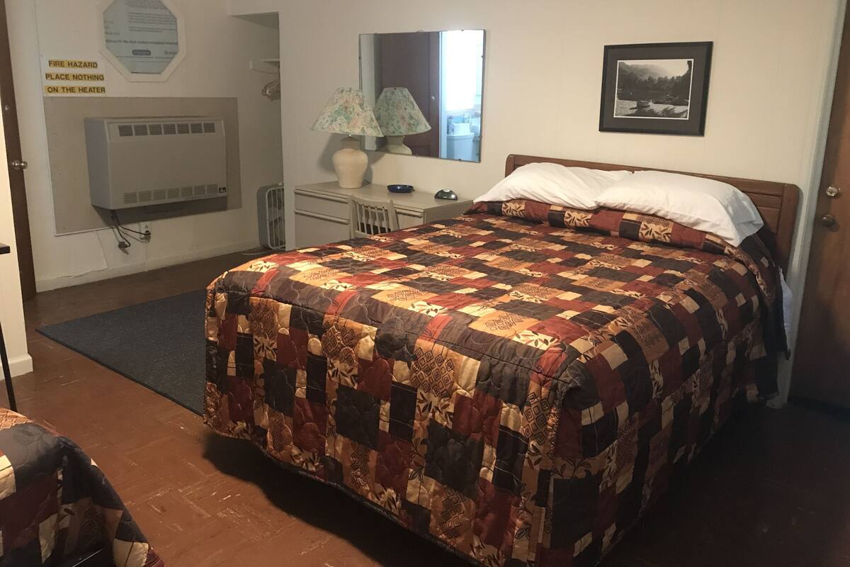 A bedroom with a large bed, a dresser, a mirror, a heater, and a fire hazard sign.
