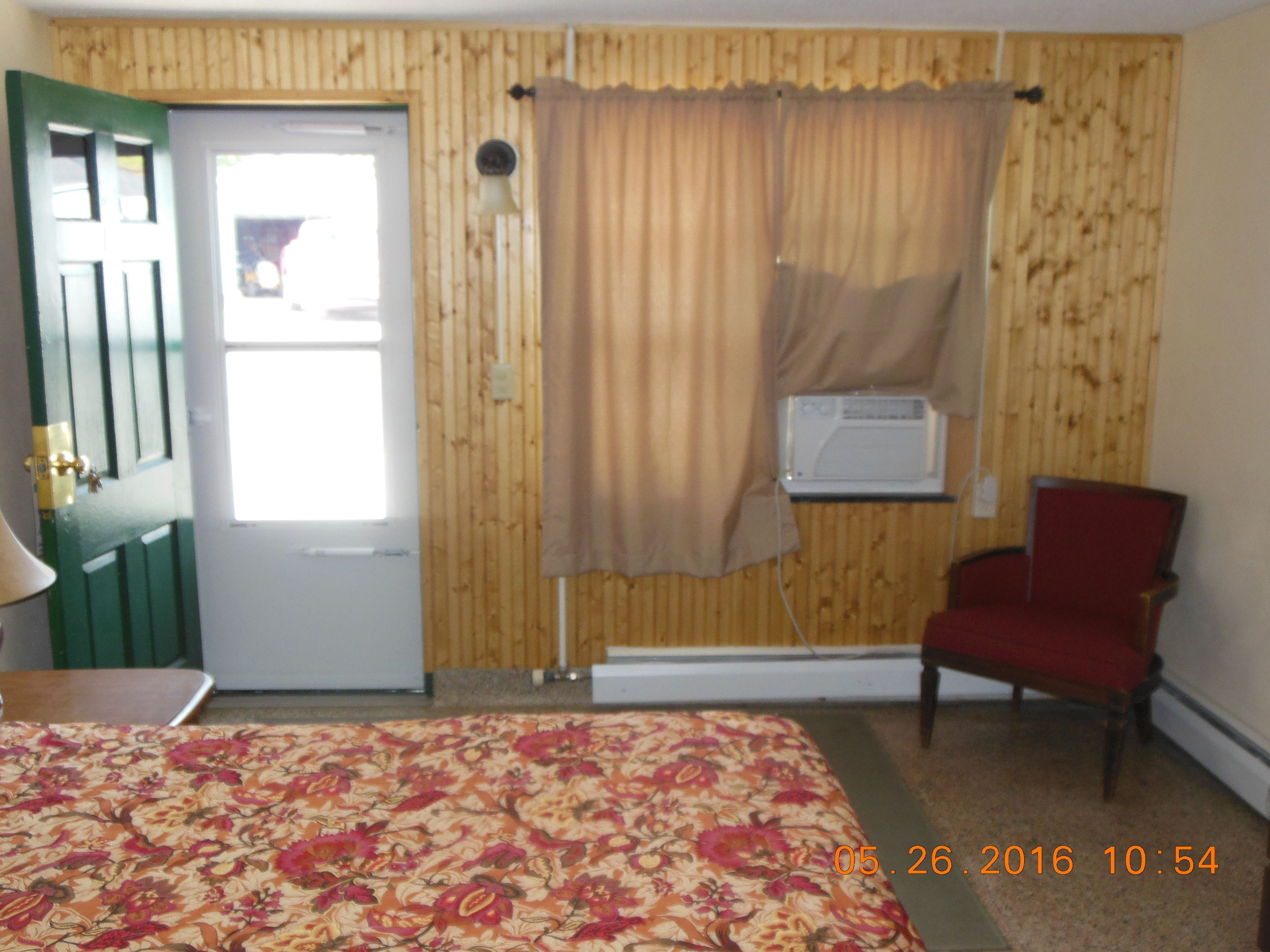 Une pièce comprenant un lit, une chaise, une porte et un appareil de climatisation.