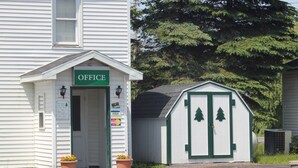 A white building with a green 'OFFICE' sign, a small shed with green trim, and two potted plants in front. - The Evergreen Motel (Oswego)