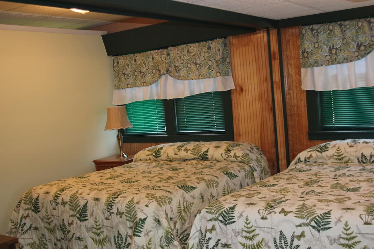 A bedroom with two beds, wooden headboard panels, green window blinds, and a patterned curtain.