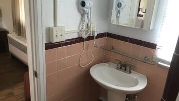 A bathroom with a white sink, a glass shelf, a hairdryer, and a mirror.